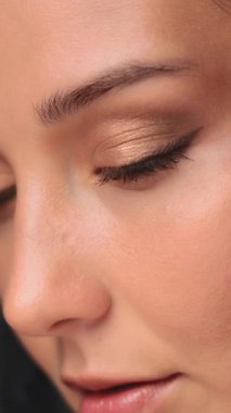 Yavaş çekim makro görüntüler, altın rengi göz farı ve pürüzsüz derisi olan bir kadının göz bölgesini gösteriyor. Kozmetik reklamları, cilt bakımı ve güzellik dersleri için ideal..