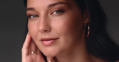 Beyaz elbiseli bir kadının yumuşak stüdyo ışığı altında nazikçe yüzünü okşamasının yavaş çekim klipsi. Güzellik ürünleri reklamları, cilt bakımı konseptleri ve modern moda kampanyaları için harika..