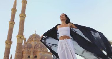 Beyaz takım elbiseli ve siyah şallı neşeli bir kadın kollarını Mısır 'ın Sharm El Sheikh kentindeki görkemli Sahaba Camii' nin yakınına açıyor. Seyahat, kültürel ve ruhsal temalar için idealdir. Yüksek kalite
