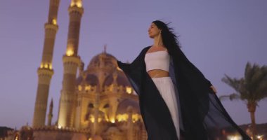 Gün batımında Sharm El Sheikh 'teki aydınlanmış Sahaba Camii' nin önünde poz veren akıcı kıyafetli zarif bir kadın. Güzelliği ve mirası vurgulayan seyahat, kültür ve yaşam tarzı terfileri için mükemmel..