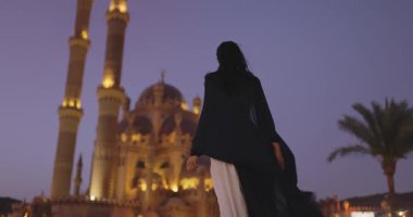 Gece karanlığında Sharm El Sheikh 'teki aydınlanmış Sahaba Camii' nden uzaklaşan akışkan elbiseli bir kadın. Güzelliği vurgulayan seyahat, kültür ve yaşam tarzı terfileri için mükemmel.