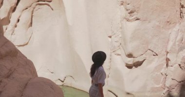 Sıradan giyinmiş bir kadın Mısır 'daki Wishwashi Kanyonu' nun kayalık duvarlarına ve dingin suyuna hayran kalıyor. Seyahat promosyonları, macera içeriği ve doğa keşfi reklamları için mükemmel..
