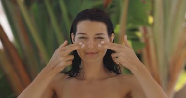 Güzel, beyaz bir kadın yüzüne nemlendirici krem sürüyordu. Cilt bakımı, güzellik, kozmetik ve tropikal sağlık yaşam tarzı içeriği için kavramsal tanıtım.