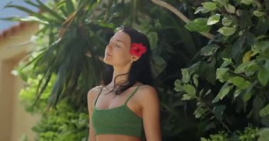 Saçında kırmızı bir çiçek olan güzel bir kadın yemyeşil bir tropikal bahçede dinleniyor. Rahatlama, doğal güzellik ve tropikal yaşam tarzları için mükemmel bir kavram. Terfi için yüksek kaliteli görüntüler. 