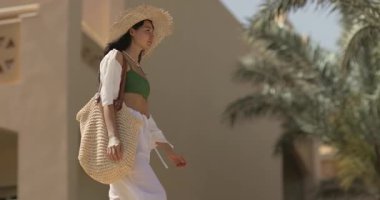 Zarif bir kadın, arka planda palmiye ağaçları olan şık kıyafetlerini sergileyerek, bir Mısır tatil köyünde ağır çekimde geziniyor. Seyahat, yaşam tarzı ve moda kavramları için mükemmel.. 