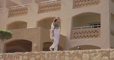 Zarif bir kadın güneşli bir günde Mısır 'da lüks bir tatil köyünü keşfediyor. Seyahat, yaşam tarzı ve moda kavramları için idealdir. Sofistike ve huzurlu bir atmosfer sunar.. 