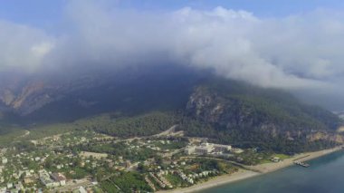 Yeşillik ve sisli dağ tepeleri tarafından çerçevelenmiş Kemer şehrinin manzaralı kıyı şeridi boyunca geniş bir hava manzarası. Turizm, seyahat konseptleri ya da tanıtım görselleri için mükemmel..