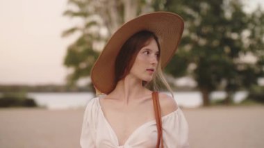 Geniş kenarlı şapkalı güzel bir kadın ve omuzsuz beyaz bir üst bakışla düşünceli bir şekilde dış mekâna bakıyor. Moda, yaşam tarzı ve seyahat promosyonları için mükemmel.
