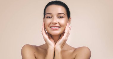 Yüzüne gülümseyen ve dokunan parlak tenli güzel bir Asyalı kadının yakın çekimi. Cilt bakımı, güzellik kavramları, reklamlar ve promosyon malzemeleri için ideal..