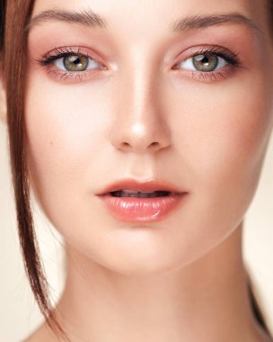 Açık tenli ve yumuşak şeftali kırmızısı makyajlı genç bir kadının stüdyo portresi. Cilt bakımı reklamları, kozmetik markalaşma ve yeni, ışıl ışıl bir stile sahip güzellik makaleleri için mükemmel..