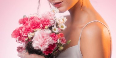 Beyaz, pembe çiçekli bir buketi nazikçe tutan genç bir beyaz kadının yakın çekimi. İlkbahar, güzellik veya yaşam tarzı reklamları için yüksek kalite romantik ve kadınsı konsept.