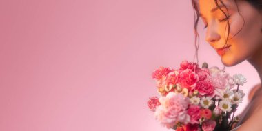 Güzel bir genç kadının romantik ve rüya gibi portresi narin çiçeklerin kokusundan nazikçe zevk alıyor. Yumuşak, pembe tonlu arka plan hassas, kadınsı atmosferi güçlendirir.