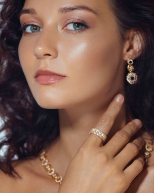 Parlak derili, altın yüzüklü, küpeli ve kolyeli kendine güvenen bir kadının zarif yakın çekimi. Moda, güzellik veya lüks mücevher promosyonları için ideal kaliteli stüdyo portresi.