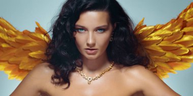 Parlak cildi, altın kanatları ve zarif takıları olan cesur üstsüz kadın stüdyoda güven içinde poz veriyor. Lüks tanıtım için yüksek kalite kavramsal moda ve fantezi imajı.