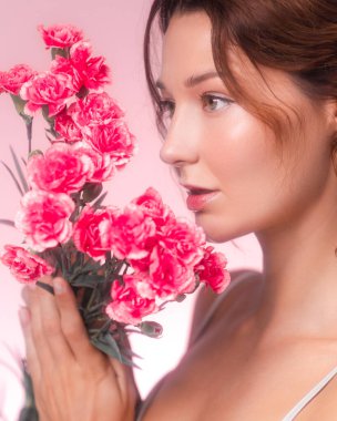 Pastel arka planda pembe karanfil tutan beyaz bir kadının yan profili. Cilt bakımı, parfüm ya da çiçek ürünleri promosyonları için kadınsı ve romantik bir görsel ideal..