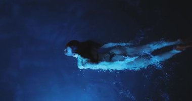 Göz kamaştırıcı bikinili bir kadın gecenin karanlığında ışıldayan mavi sularda zarafetle yüzer. Gerçeküstü ışık ve akışkan hareket rüya gibi, gizemli ve sinematik bir sualtı sahnesi yaratır.. 