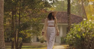 Hasır şapkalı, açık renk elbiseli, güzel bir kadın taze hindistan cevizi taşıyan, tropikal bir bahçede geziniyor. Rüya gibi bir sahne. Yazı, doğayı ve seyahat titreşimlerini yakalıyor.. 