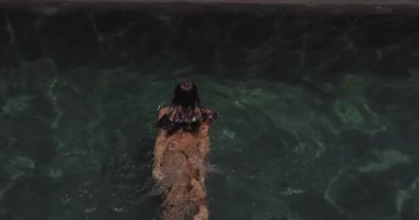 Çarpıcı bir bikini modeli, lüks bir açık havuzda şehvetli bir yüzüşten zevk alır. Islak teni, tropik bir cennette suda zarifçe ilerlerken güneş ışığında parlıyor.. 