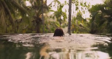 Bikinili sakin bir kadın sonsuz bir havuzun kenarına yaslanır ve ormanın sakin ortamının tadını çıkarırken gülümser. Bu sahne rahatlamayı, lüksü ve barışçıl bir tropikal kaçışı simgeliyor..