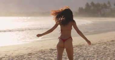 Kırmızı bikinili kaygısız bir kadın gün batımında Dickwella Sahili, Sri Lanka 'nın altın kumları boyunca yürüyor ve oynuyor. Seyahat, yaşam tarzı ve tropikal tatil temaları için ideal. 