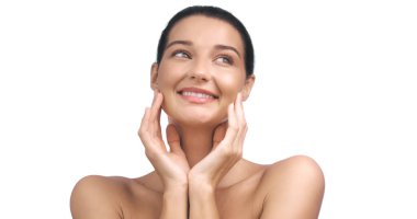 Yüzüne dokunurken sevinçle gülümseyen kusursuz, parlak ciltli beyaz bir kadın. Reklamlarda ve reklamlarda cilt bakımı, güzellik ve refah kavramları için idealdir.. 