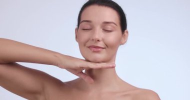 Beyaz arka planda kapalı gözler ve ince çene dokunuşu ile güzel beyaz model poz verir. Sağlık, güzellik rutini, kadınsı cilt bakımı ve kişisel bakım içeriği için ideal..