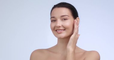 Çıplak yüzlü beyaz kadın, sakin bir gülümsemeyle yanağını nazikçe okşuyor. Üst düzey güzellik markaları, spa tedavileri, cilt bakımı ve lüks sağlık reklamları için idealdir..