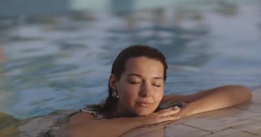 Huzurlu bir kadın güneşli yüzüyle havuzda huzurlu bir anın tadını çıkarıyor. Yaşam tarzı, sağlık ve seyahat, rahatlama, güzellik ve memnuniyeti ön plana çıkarmak için ideal..