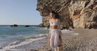 Kayalık bir plajda arka planda yükselen sahil kayalıkları olan, güneş ışığıyla yıkanan bir kadın. Bu görüntüler macera, kıyı yaşam tarzı ve doğal güzellik kavramları için idealdir..