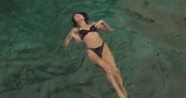 Sakin bir tropikal havuzda yüzen siyah bikinili bir kadının huzurlu anı. Lüks seyahatler, yaz tatili rahatlığı ve egzotik tatil görüntüleri için ideal..