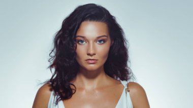 Parlak tenli, doğal makyajlı ve Yunan tarzı beyaz elbiseli bir kadının stüdyo güzelliği. Cilt bakımı, moda, yazı işleri ve lüks kozmetik endüstrisi promosyonları için ideal..