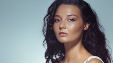 Işık saçan cildi ve yumuşak makyajı olan kendine güvenen bir kadının stüdyo yakın çekimi. Temiz ve minimal bir düzende çekilmiş. Cilt bakımı, moda, güzellik ve kozmetik endüstrisi promosyon içeriği için ideal.