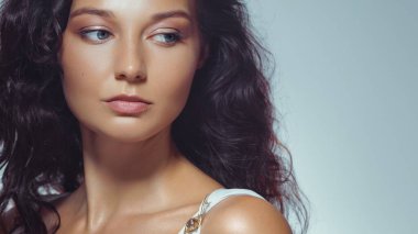 Zarif esmer, yumuşak makyajlı ve parlak tenli bir kadın yan tarafa bakıyor. Moda, cilt bakımı, dergi kapakları veya modern güzellik reklam kampanyaları için stüdyo portresi konsepti.