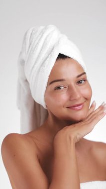 Temiz tenli ve kafasında havlu olan güzel beyaz kadın cilt tanıtımında yüzüne nazikçe dokunur. Güzellik, kozmetik, sağlık ve reklam kullanımı için ideal kavramsal görüntüler.