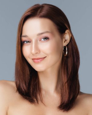 Sağlıklı, beyaz tenli ve düz kahverengi saçlı güzel bir kadın. Stüdyoda hafifçe gülümsüyor. Cilt bakımı, kozmetik ürünleri, sağlık ürünleri veya saç bakım ürünleri için mükemmel..