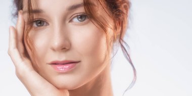 Doğal makyajlı, parlak tenli, yüzüne hafifçe dokunan genç bir kadının zarif yakın çekimi. Cilt bakımı markaları, temiz güzellik kampanyaları ve sağlık yaşam tarzı kavramları için ideal..