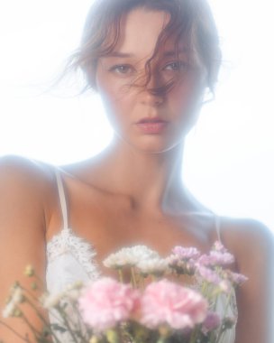 Beyaz bir kadının romantik portresi. Pastel çiçekleri yumuşak ışıkta tutuyor. Aşk, güzellik, kadınsı zarafet ve çiçek reklamı için kavramsal imaj. Reklamlar ve afişler için ideal.