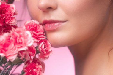 Yumuşak pembe karanfil çiçekleriyle genç bir kadının alt yüzü ve dudaklarının şehvetli yakın çekimi. Kozmetik reklamları, sağlık ve romantik görseller için estetik güzellik ve cilt konsepti.
