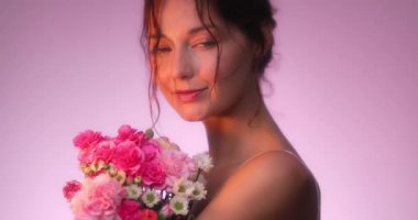 Parlayan pembe ışıkta canlı bir buket pembe çiçeği kucaklayan ve koklayan muhteşem bir Kafkas modeline yakın çekim. Parfüm reklamları, romantizm, sağlık ve çiçek ürünleri için mükemmel..