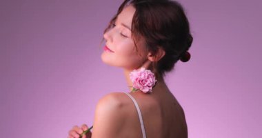 Omzunda pembe bir çiçekle romantik poz veren beyaz bir kadının yavaş çekim görüntüleri. Koku, güzellik ve cilt ticareti için ideal..