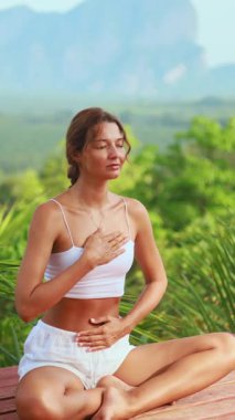 Sağlıklı bir kadının tropik yeşilliklerle çevrili nefes farkındalığı pratiği yaptığı huzurlu bir yoga sahnesi. Sağlık, sağlık, zindelik ve yaşam tarzı reklamcılığı veya tasarımı için harika..
