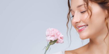 Kapalı gözlü, mutlu bir gülüşü olan pembe çiçekli genç bir kadının yumuşak afişi. Cilt bakımı, güzellik ürünleri, çiçek parfümü reklamları ve sağlık temalı promosyonlar için mükemmel..