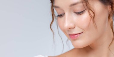 Beyaz tenli, parlak cilt ve doğal makyajla gülümseyen genç bir kadının yakın çekimi. Temiz stüdyo ışığı altında çekilmiş. Cilt bakımı, sağlık ve güzellikle ilgili görseller için mükemmel..