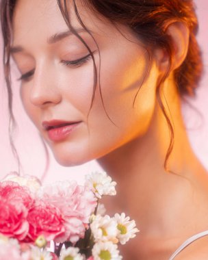 Işıl ışıl cildi ve gözleri kapalı, pembe ve beyaz çiçekleri koklayan genç bir kadının yakın çekimi. Cilt bakımı, çiçek kokusu ya da romantik güzellik kampanyaları için ideal..