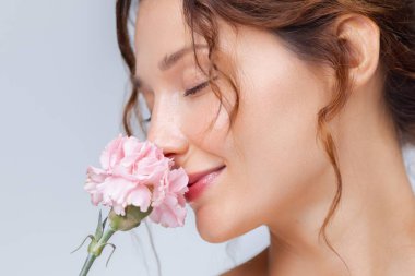 Doğal makyajlı, parlak tenli, pembe karanfil kokan beyaz bir kadının yakın çekimi. Güzellik, cilt bakımı, sağlık ve çiçek temalı tanıtım içeriği için ideal..