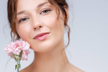 Beyaz tenli ve doğal makyajlı yumuşak pembe karanfilli genç bir kadının yakın çekim portresi. Cilt bakımı reklamları, kozmetik ürünleri, sağlık ve güzellik markaları için mükemmel..