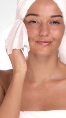 Spa havlusu içindeki beyaz kadın makyajı mendille nazikçe temizliyor ve parlak tenine dokunuyor. Güzellik reklamları, cilt rutinleri, yüz bakımı ve sağlıklı yaşam için ideal..
