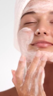 Kafasında havlu olan beyaz bir kadın nazikçe cildine köpük temizleyici sürüyor. Yüz bakımı, cilt bakım ürünleri, güzellik dersleri ve sağlık reklamları için ideal bir konsept..