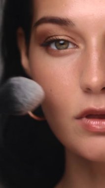 Kafkasyalı bir kadının fırçayla makyaj yaparken yakın çekimi. Parlak cilt ve altın göz farı kozmetik tanıtım ve cilt bakımı için mükemmel kaliteli bir güzellik konsepti yaratır..