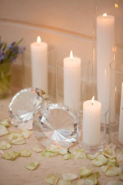 Cam tutacaklarda beyaz mumlar dağınık gül yaprakları ve parlak kristal süslemeler. Düğünler ve özel etkinlikler için romantik ve lüks bir ortam yaratmak için ideal..